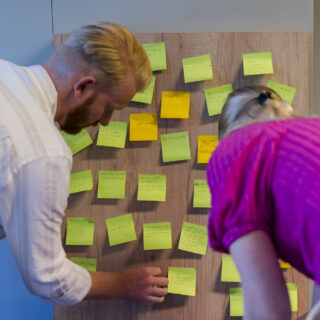 Deelnemers plakken post it op een muur tijdens een workshop